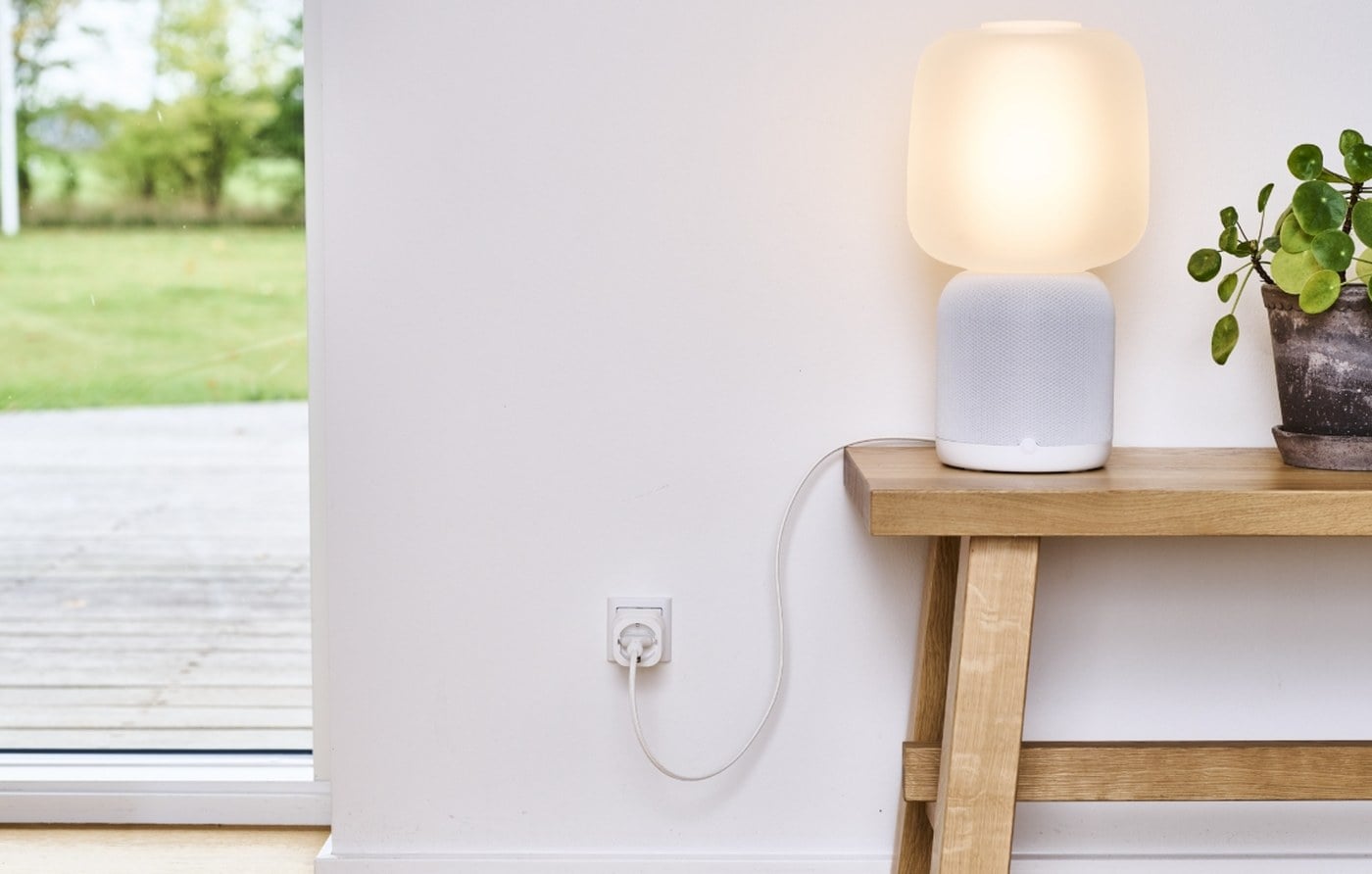 SikkertHjem S7pro Smart Plug i en stikkontakt med en tændt bordlampe på en konsol